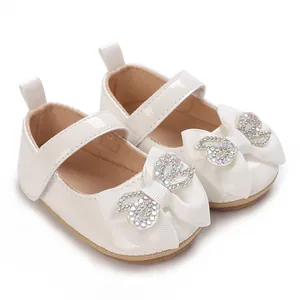Close-up detail of white patent leather baby princess shoes with sparkling rhinestone bow