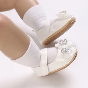 Close-up of white baby girl Mary Janes with satin bow and sparkling rhinestone detail