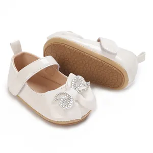 Close-up detail of white baby girl walking shoes with a sparkling rhinestone bow decoration