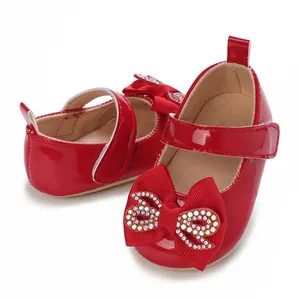 Close-up view of red patent leather baby girl Mary Jane shoes featuring a rhinestone bow