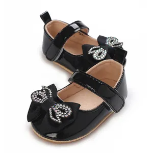 Close-up detail of black patent baby walker shoes featuring a sparkling rhinestone bow tie