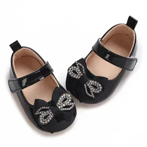 Close-up detail of black patent baby walker shoes with rhinestone bows and soft soles.
