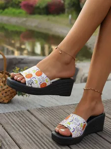 Stylish women's wedge sandals with Halloween pumpkin print worn outdoors on a wooden deck