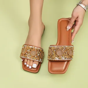 Detail van glinsterende strass- en kralenmotieven op bruine platte slippers met vierkante neus