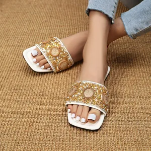 Detailopname van witte platte sandalen met vierkante neus en gouden strass-details
