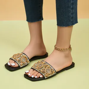 Detail van platte damesslippers met vierkante neus en gouden strass- en kralenborduursel