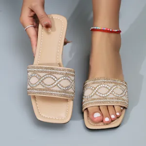 Detailoverzicht van beige platte sandalen met vierkante neus en decoratieve strasspatronen.