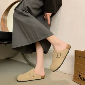 Close-up detail of stylish beige suede backless clogs with a cork footbed and buckle strap