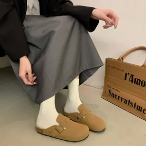 Close-up of brown suede clogs with buckle strap and cork sole worn with socks.