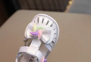 Dettaglio di sandalo bianco per bambina con decorazione a fiocco e girandola colorata.