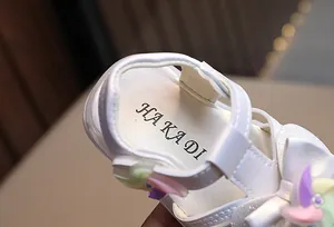 Dettaglio di sandalo bianco per neonata con girandola e logo HAKADI