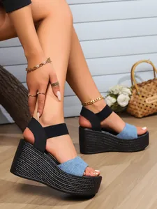 Detail shot of blue denim platform wedge sandals with black elastic ankle straps