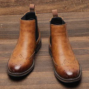 Vista detallada de botas Chelsea Brogue de cuero marrón vintage para hombre en madera.