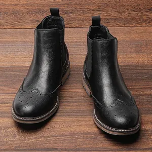 Botines Chelsea clásicos de cuero negro con detalles brogue sobre madera