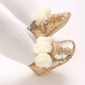 Detailansicht goldener Babyschuhe mit Glitzer und einer eleganten weißen Blume