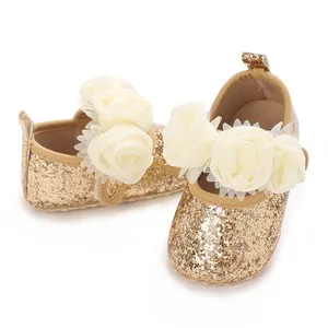 Makroansicht von goldenen Glitzer-Babyschuhen mit eleganten weißen Rosenblumendekorationen