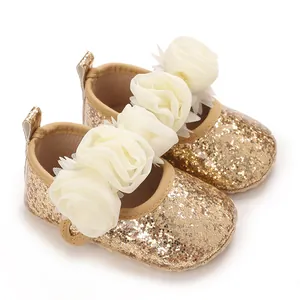 Nahaufnahme von goldglitzernden Baby-Lauflernschuhen mit cremefarbenen Stoffblumen