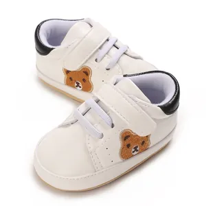 Detailopname van witte babyschoentjes met schattige berenborduring en zachte zolen.