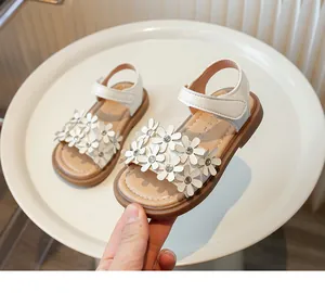 Close-up of white girls' sandals featuring elegant 3D flower and rhinestone details.