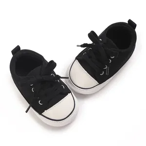 Gros plan de baskets classiques pour bébés, chaussures souples noires et blanches.