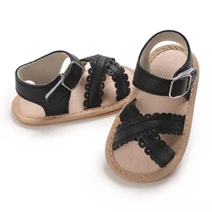 Close-up of baby girl sandals with black scalloped cross straps and soft tan soles