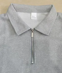 Vue détaillée polo gris en maille gaufrée avec fermeture éclair et étiquette 100 % polyester