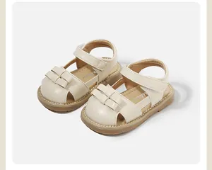 Cream leather baby girl sandals with decorative bow and velcro strap detail.