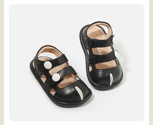 Vista detallada de sandalias de cuero negro para bebé con botones blancos decorativos.