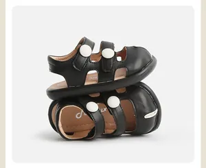 Primer plano de sandalias negras para niños con botones blancos y correas ajustables.