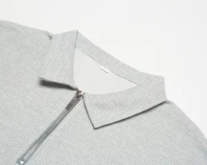 Vue détaillée d'un polo gris clair en maille gaufrée montrant le col zippé et la texture