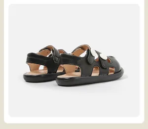Detalle lateral de sandalias de verano negras para niños pequeños con botones blancos