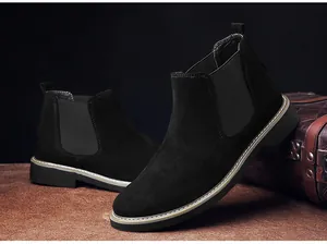 Detailansicht schwarzer Chelsea-Boots aus Wildleder für Herren vor einem Lederkoffer-Dekor.