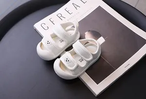 Close-up of white breathable mesh baby sandals with cute bear detail on a magazine background.