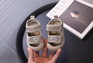 Close-up of beige breathable mesh baby sandals with cute bear patch decoration.