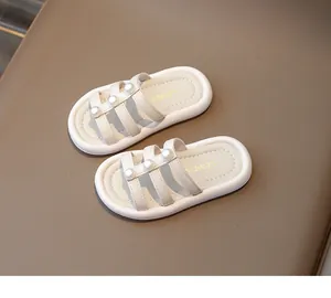 Detalle de sandalias crema para niña con tres tiras adornadas con perlas y suela suave.