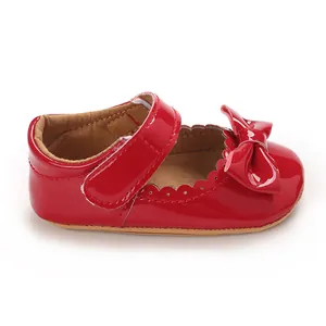 Vista detallada de un zapato de bebé en charol rojo brillante con un gran lazo elegante