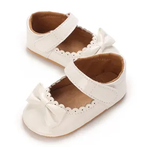 Primer plano de zapatos de charol blanco para bebé con lazo y bordes festoneados