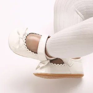 Detalle de zapatos Mary Jane para bebé en PU blanco con lazo y borde festoneado.