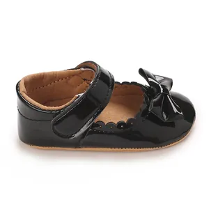 Vista detallada de zapatos de charol negro para bebé con lazo y bordes festoneados