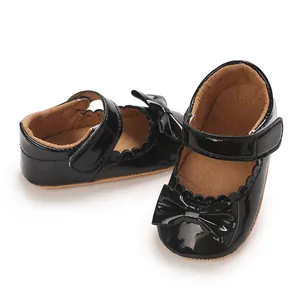 Vista detallada de zapatos de charol negro para bebé con lazo y tira de velcro