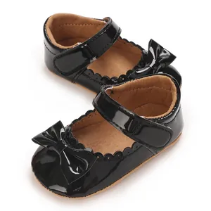 Primer plano de zapatos de charol negro para bebé con lazo y borde festoneado.