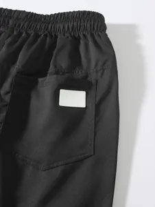 Close-up detail of the back pocket and blank white label on black woven beach shorts.