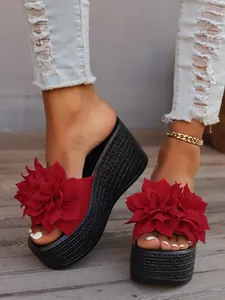 Close-up detail of red floral wedge platform sandals with black woven soles on wooden background