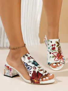 Close-up of women's white sandals with floral embroidery and rhinestone chunky heels