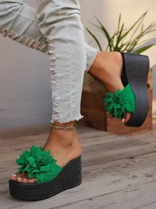 Detailed close-up of green wedge platform sandals with 3D fabric flower on wooden deck