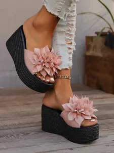 Close-up of pink fabric flower wedge sandals with black platform sole on a model