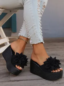 Close-up detail of black platform wedge sandals featuring 3D decorative fabric flowers