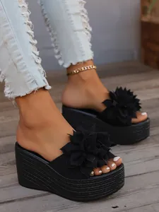 Close-up view of black platform wedge sandals featuring a large decorative flower detail