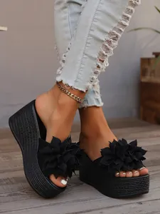 Detail of black platform wedge sandals featuring large fabric floral accents on the vamp