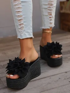 Detailed shot of black wedge platform slippers with decorative 3D fabric flowers on feet